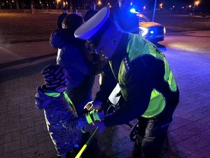 Kolorowe zdjęcie policjanta Ruchu Drogowego, który chłopczykowi zakłada na przedramię opaskę odblaskową