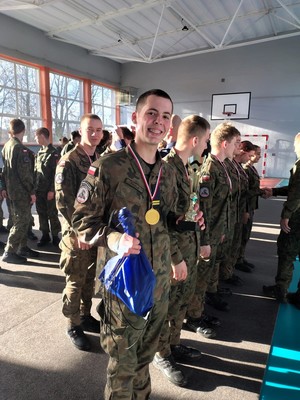 Kolorowe zdjęcie uśmiechniętego uczestnika konkursu stojącego w umundurowaniu moro. W ręce trzyma worek z gadżetami, które otrzymał od policjanta.