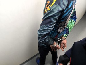 Kolorowe zdjęcie mężczyzny stojącego w kajdankach założonych na ręce trzymane z tyłu.