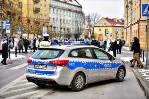 Kolorowe zdjęcie oznakowanego radiowozu na tle osób uczestniczących w orszaku.