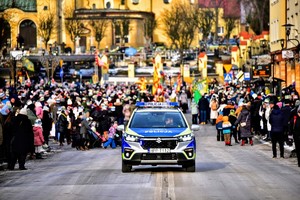 Kolorowe zdjęcie oznakowanego radiowozu na tle osób uczestniczących w orszaku.