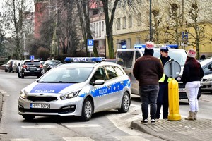 Kolorowe zdjęcie oznakowanego radiowozu Policji oraz umundurowanego policjanta rozmawiającego z dwoma uczestnikami orszaku.