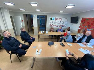 Kolorowe zdjęcie umundurowanych policjantów oraz seniorów siedzących przy stole.