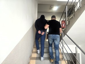 Kolorowe zdjęcie nieumundurowanego policjanta prowadzącego po schodach komendy Policji zatrzymanego mężczyznę.