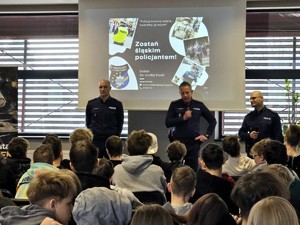 Kolorowe zdjęcie umundurowanych policjantów prowadzących wykład przed młodzieżą ósmych klas szkół podstawowych.