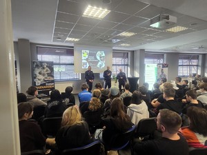 Kolorowe zdjęcie umundurowanych policjantów prowadzących wykład przed młodzieżą ósmych klas szkół podstawowych.