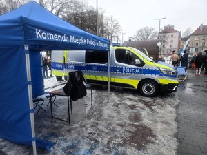 Kolorowe zdjęcie stoiska profilaktyczo-edukacyjnego Policji, na którym widać Namiot Komendy Miejskiej Policji oraz oznakowany radiowóz.