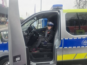 Kolorowe zdjęcie uśmiechniętej dziewczynki która siedzi w oznakowanym radiowozie na miejscu kierowcy w czapce drogówki.