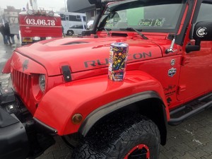 Kolorowe zdjęcie samochodu terenowego na którego nadkolu stoi puszka Wielkiej Orkiestry Świątecznej Pomocy.