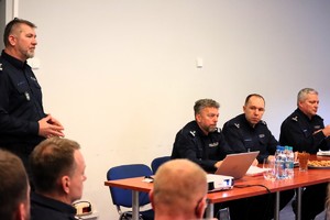 Kolorowe zdjęcie komendantów siedzących przy stole podczas przemówienia Komendanta Miejskiego Policji w Tychach.