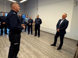 Kolorowe zdjęcie Komendanta Miejskiego Policji w Tychach żegnającego policjanta odchodzącego na emeryturę. W tle widoczna kadra kierownicza Komendy.
