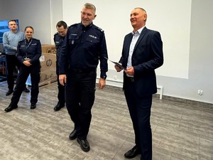 Kolorowe zdjęcie Komendanta Miejskiego Policji w Tychach żegnającego policjanta odchodzącego na emeryturę. W tle widoczna kadra kierownicza Komendy.
