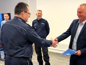 Kolorowe zdjęcie Naczelnika Wydziału Prewencji Komendy Policji w Tychach podającego dłoń odchodzącemu na emeryturę Policjantowi. W tle uśmiechnięty Komendanta Miejski Policji w Tychach.