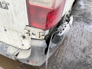 Kolorowe zdjęcie samochodu typu bus na którym widoczny jest jego zły stan techniczny. Wykonane zbliżenie uszkodzonego klosza tylnej lampy.