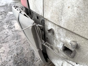 Kolorowe zdjęcie samochodu typu bus na którym widoczny jest jego zły stan techniczny. Zdjęcie wykonane w zbliżeniu uszkodzonego tylnego zderzaka.