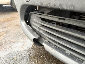 Kolorowe zdjęcie samochodu typu bus na którym widoczny jest jego zły stan techniczny. Wykonano zbliżenie na uszkodzony przedni zderzak.