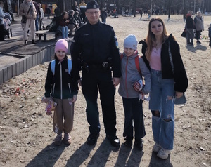 Kolorowe zdjęcie umundurowanego policjanta stojącego z kobietą i dwojgiem dzieci.