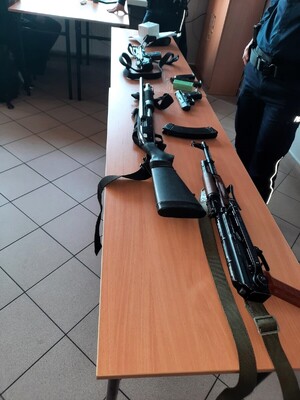 Kolorowe zdjęcie stołu na którym ułożone są jednostki broni palnej krótkiej i długiej.