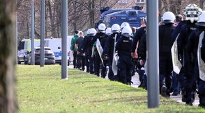 Kolorowe zdjęcie policjantów Oddziałów Prewencji Policji ubranych w kaski i wyposażonych w tarcze konwojujący kibiców.