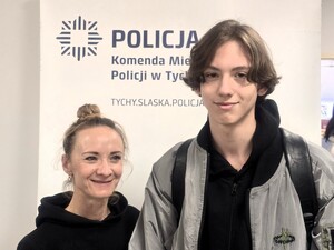 Uśmiechnięci kobieta i mężczyzna na tle baneru promocyjnego Policji.
