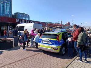 Dwa oznakowane radiowozy Policji, w pobliżu których znajdują się dzieci z opiekunami. W tle widać budynek Mediateki.