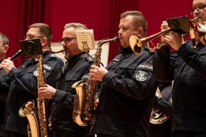 Policjanci orkiestry w mundurach policyjnych stojący z instrumentami na scenie.