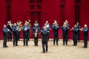 Policjanci orkiestry w mundurach policyjnych stojący z instrumentami na scenie.
