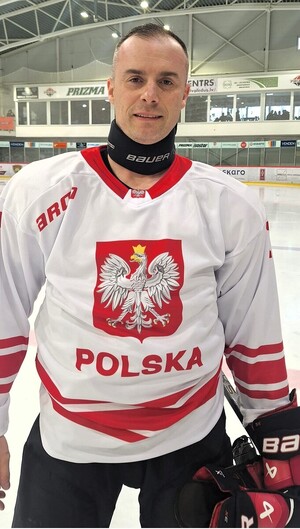 Zawodnik drużyny ubrany w strój hokejowy stojący na tafli stadionu zimowego.