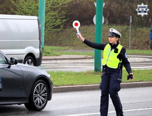 Umundurowana policjantka drogówki wchodzi na jezdnie z podniesioną tarczą do zatrzymywania pojazdów.