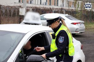 Policjantka stojąca przy zatrzymanym do kontroli samochodzie.