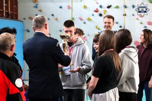 Komendant Komendy Miejskiej Policji w Tychach mł. insp. Tomasz Zawadzki wręczający uczniom puchar.
