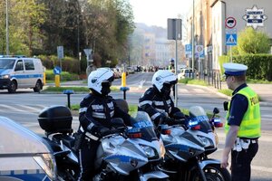 Umundurowani policjanci tyskiej drogówki, dwoje z nich ubranych jest w kombinezony policyjne motocyklowe, którzy siedzą na oznakowanych motocyklach.
