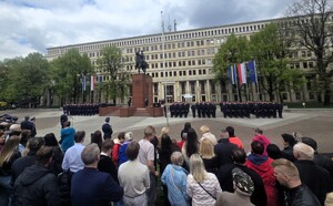 Osoby cywilne, w tle widoczni nowo przyjęci policjanci stojący przy pomniku Józefa Piłsudskiego.