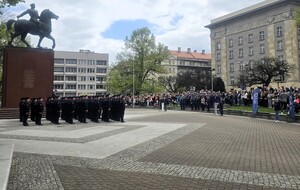 Policjanci stojący na placu, w pobliżu goście honorowi oraz widownia.