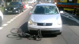 Samochód osobowy marki Volkswagen Polo ze stłuczoną szybą stojący na jezdni. Pod prawym narożem samochodu widoczny jest zniszczony rower.