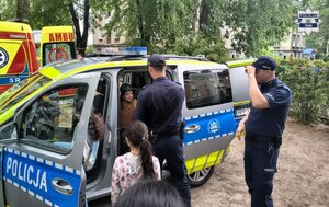 Umundurowani policjanci przy oznakowanym radiowozie podczas prezentacji dla uczestników wydarzenia.
