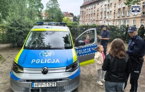 Umundurowani policjanci przy oznakowanym radiowozie podczas spotkania z dziećmi.