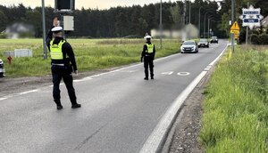 Umundurowani policjanci Wydziału Ruchu Drogowego stoją na jezdni, w tle widoczne nadjeżdżające pojazdy.