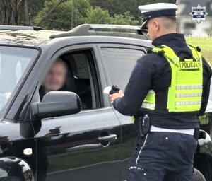 Umundurowany policjant Wydziału Ruchu Drogowego przeprowadzający badanie stanu trzeźwości kierującego samochodem osobowym.