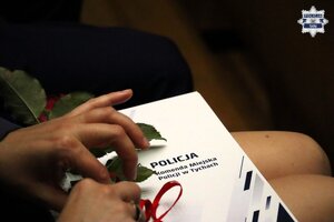 Policjantka trzymająca na kolanach teczkę z aktem mianowania oraz różę.