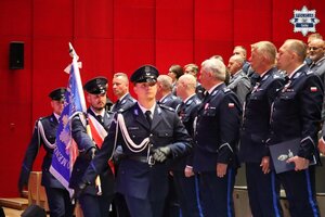 Policjanci pocztu sztandarowego podczas wyprowadzania sztandaru. W tle widać umundurowanych policjantów kadry kierowniczej.