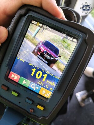 Wyświetlacz ręcznego miernika prędkości na którym widoczny jest samochód marki BMW oraz wskazania cyfrowe w tym prędkości, to jest 101 km/h.