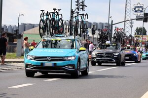 Jadące jezdnią samochody serwisowe wyścigu z rowerami przewożonymi na bagażnikach dachowych.