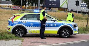 Umundurowani policjanci stoją obok oznakowanego radiowozu Policji.