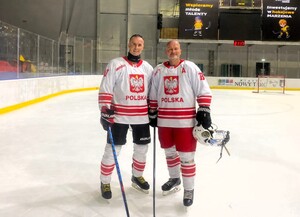 Dwóch mężczyzn ubranych w stroje hokejowe stojące na stadionie zimowym.