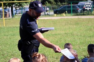 Policjant wręczający kolorowanki dzieciom.