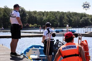 Policjant stojący na pomoście jeziora w pobliżu łodzi policyjnej oraz ratownika WOPR.