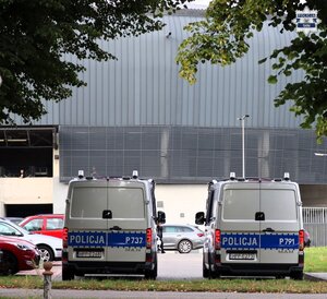Oznakowane radiowozy policyjne stojące na parkingu. W tle widoczny stadion miejski.