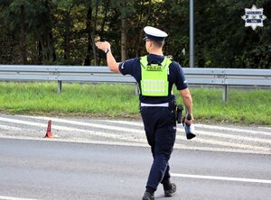 Umundurowany Policjant Wydziału Ruchu Drogowego wchodzący na jezdnię w celu zatrzymania pojazdu do kontroli.