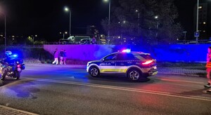 Oznakowany radiowóz z włączonymi sygnałami świetlnymi oraz motocykle policyjne podczas zabezpieczenia przejazdu osób na łyżworolkach.